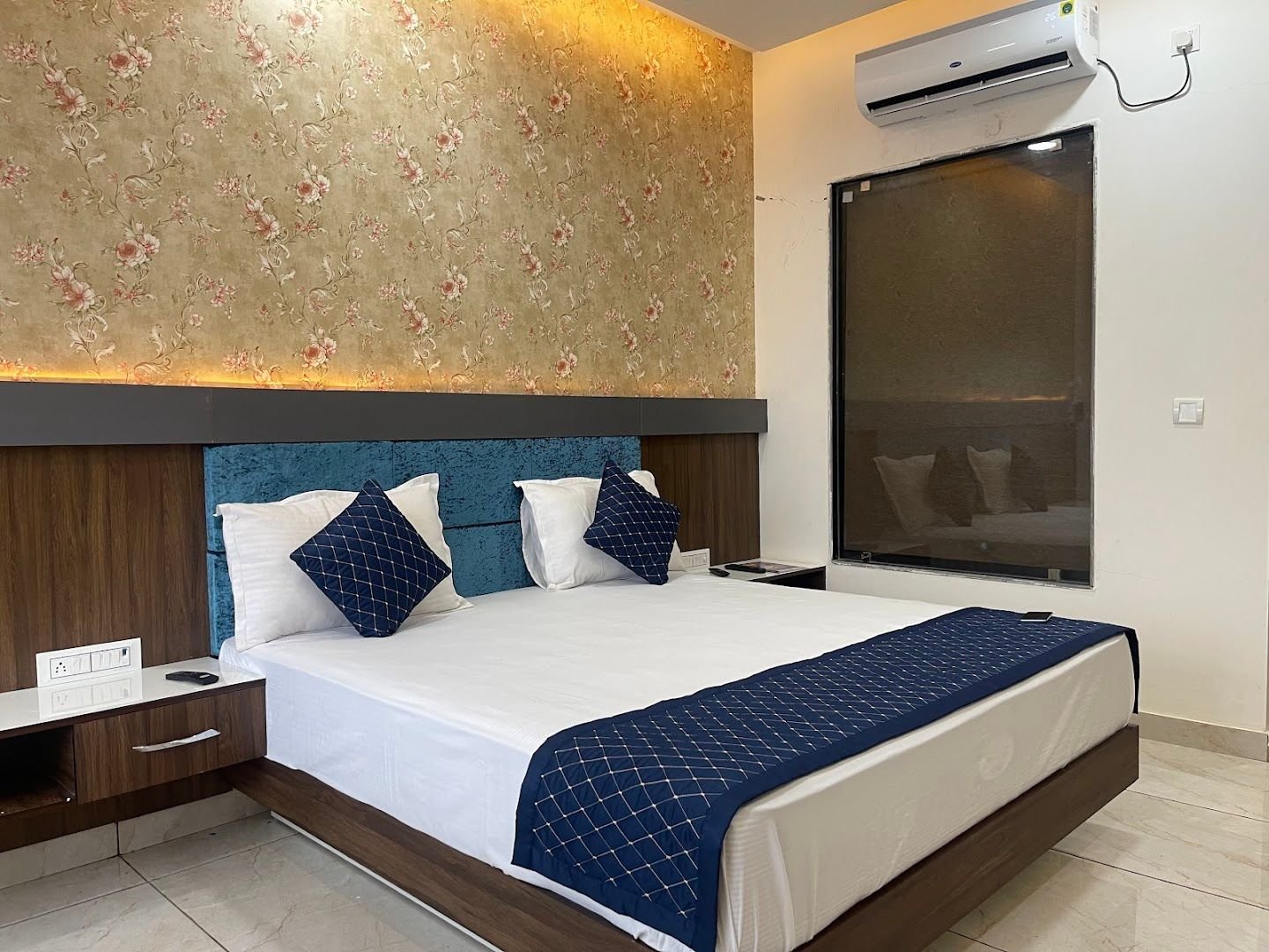 Double bed with blue cushions, floral wallpaper and air conditioning
